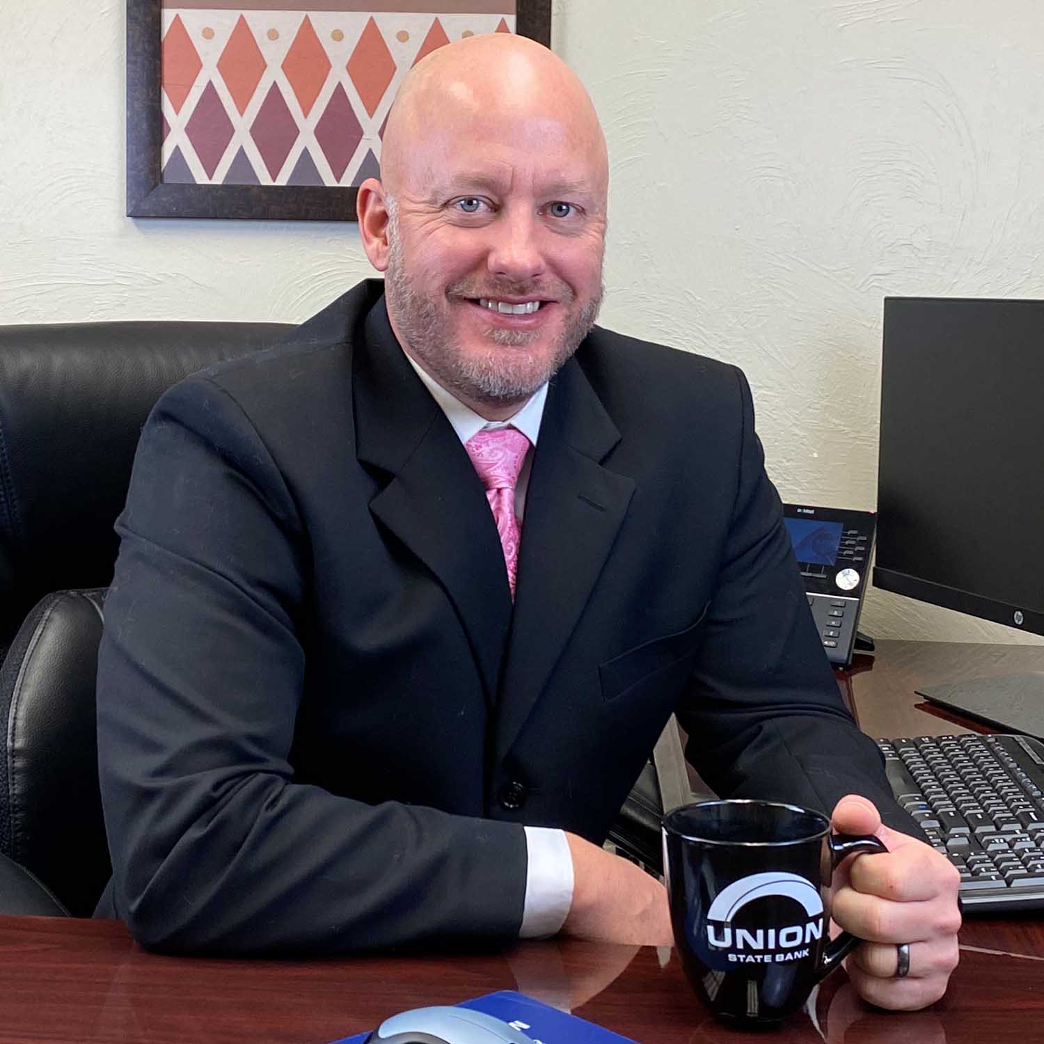 Photo of Zack Stoy, lender with Union State Bank, sitting at desk holding a coffee mug.