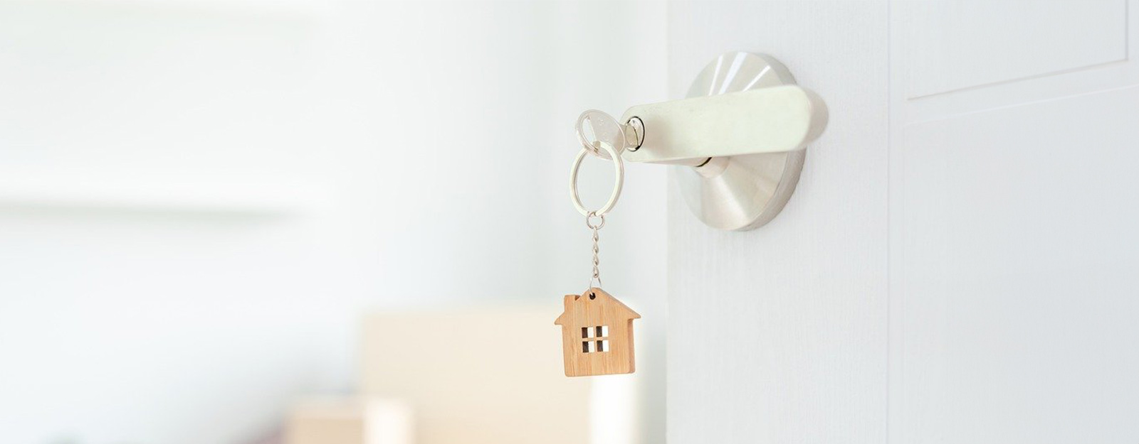 Image of an open door with a key in the lock. Key is connected to a house shaped cutout made of wood. 