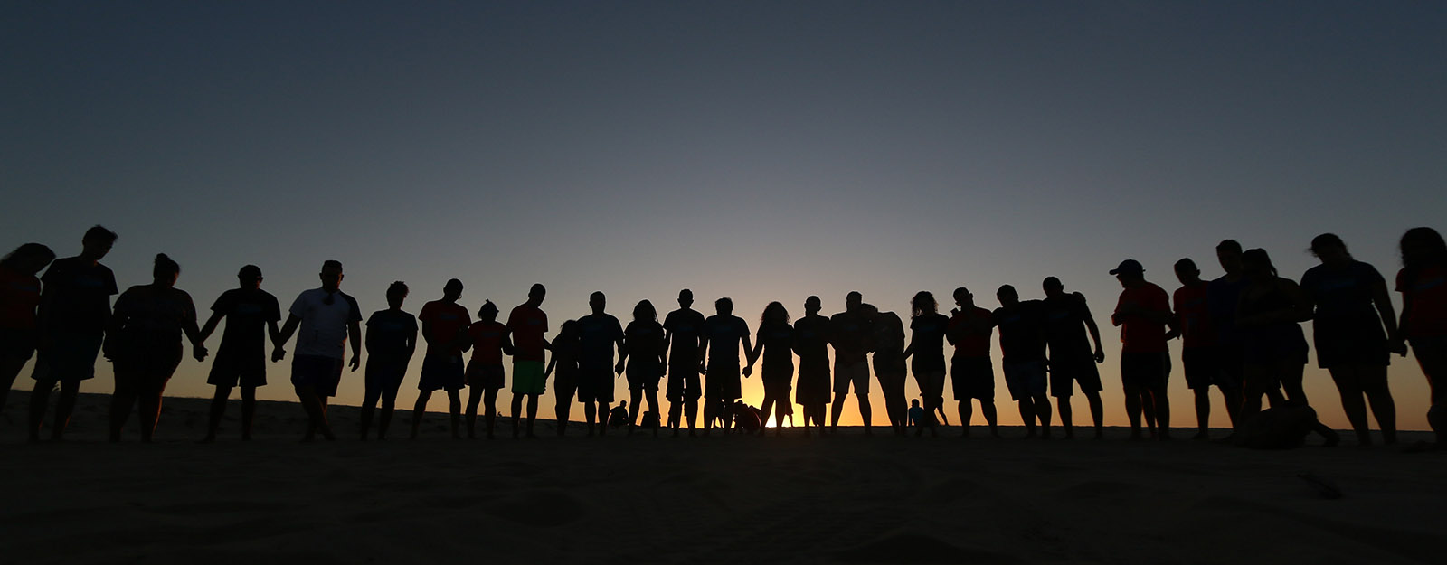 Photo silhouette of a large group holding hands in a line while the sunsets behind them.